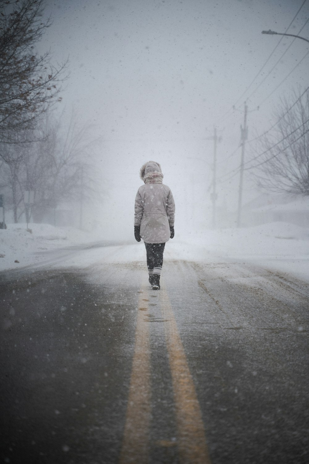 woman in white coat walking on snow covered road during daytime