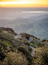 A scenic winding road through a lush green Spanish countryside at sunset.