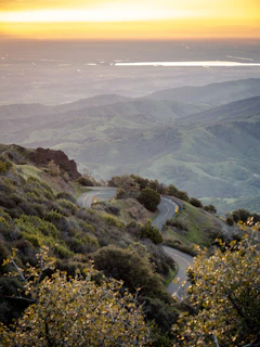 Winding mountain road cutting through lush green hills at sunset.