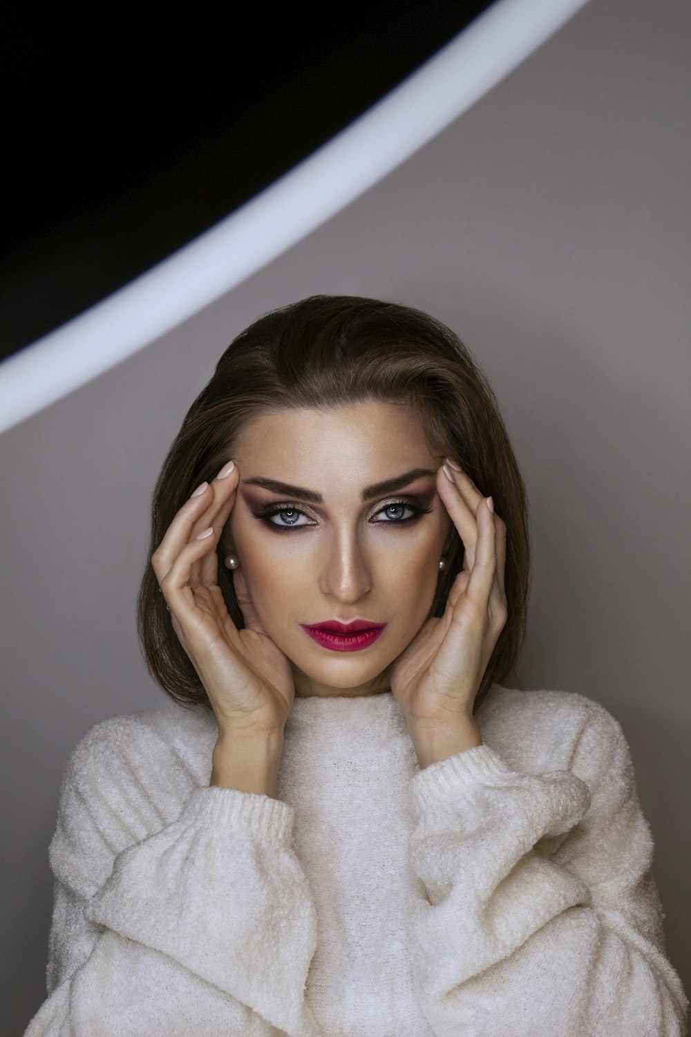 woman in white sweater holding her face