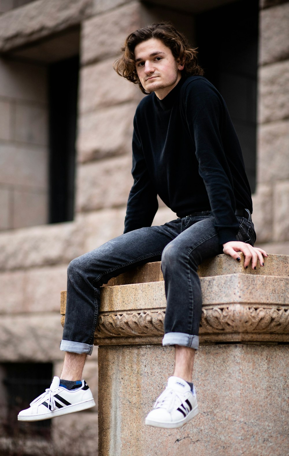 man in black zip up jacket and blue denim jeans sitting on brown concrete bench during