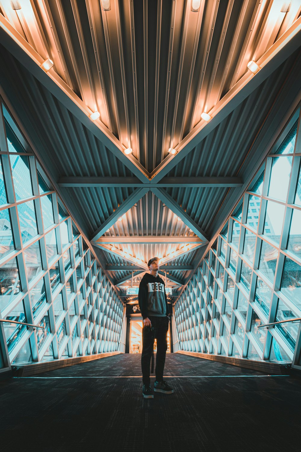 man in black jacket and black pants standing on blue glass walled building