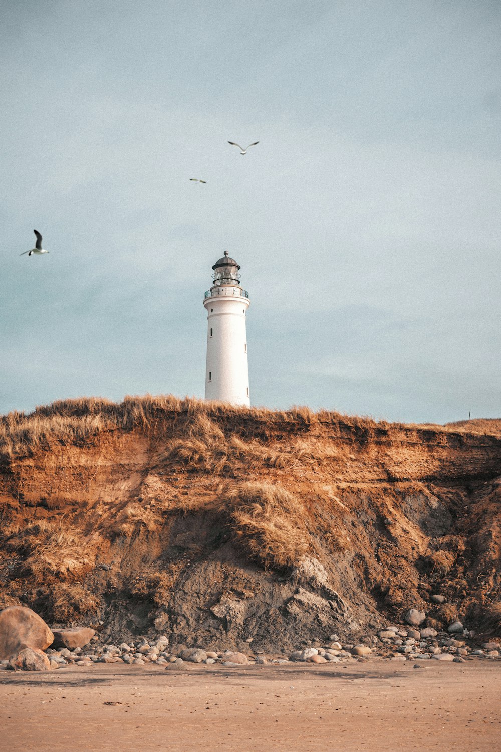 white lighthouse on brown hill under white clouds during daytime