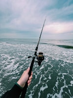 An angler holding a freshly caught fish by the sea, with waves in the background.