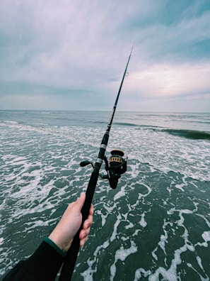 An angler holding a freshly caught fish by the sea, with waves in the background.