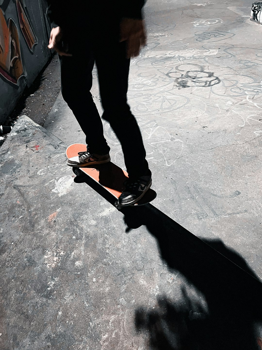 person in black pants and black and orange sneakers standing on gray concrete floor