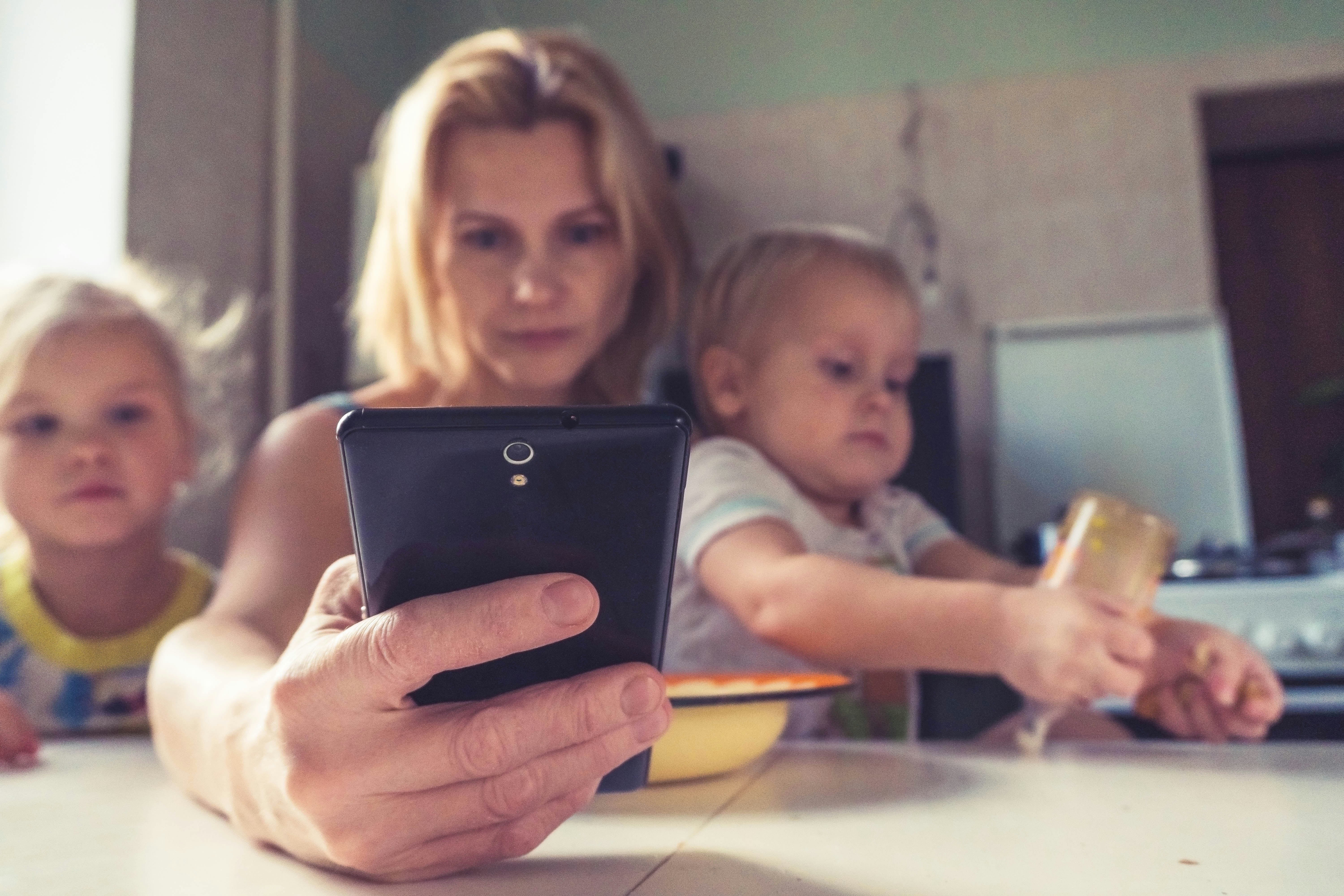 A woman uses smartphone while sitting with children, working mom