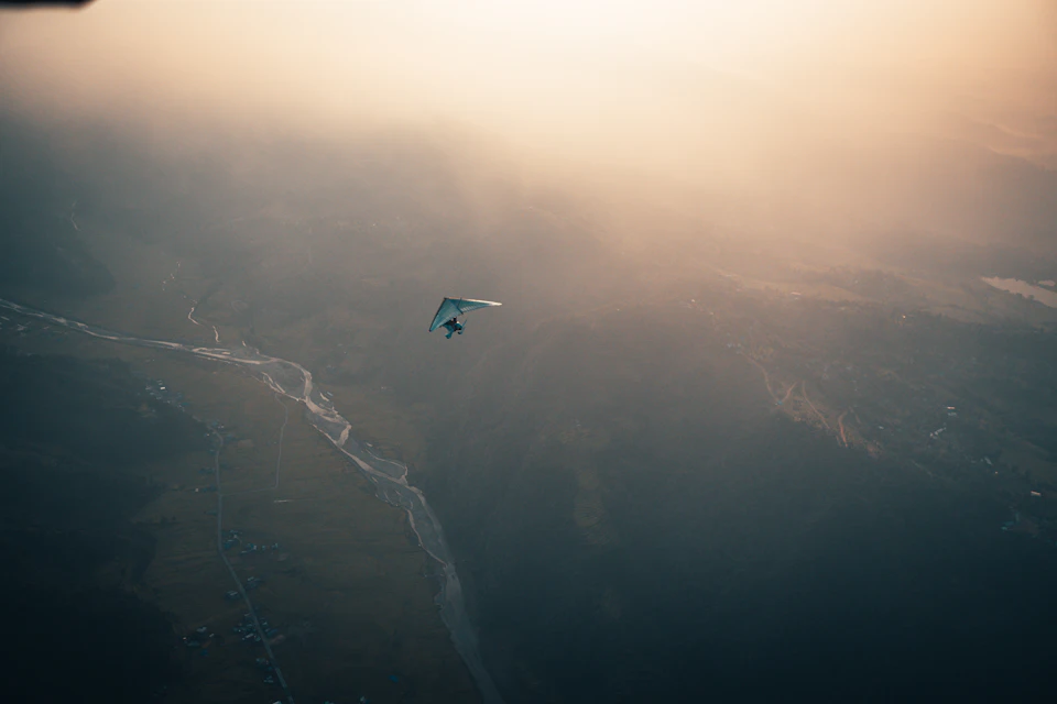 Person glides on kite in the sky, arms extended for balance, soaring above landscape