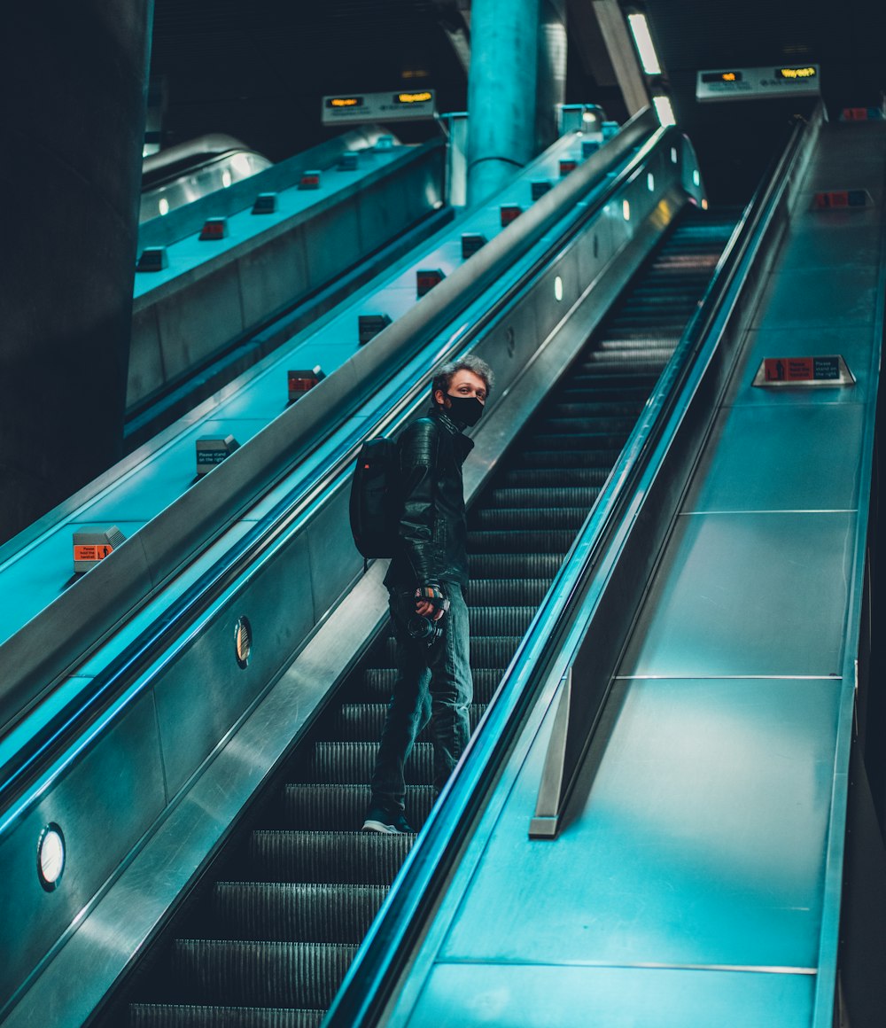 man in black jacket and black pants walking on escalator