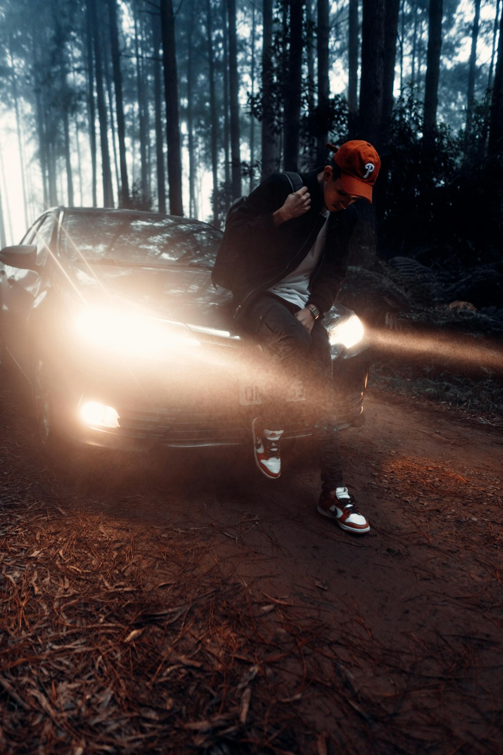 man in black jacket and orange helmet sitting on car hood during daytime