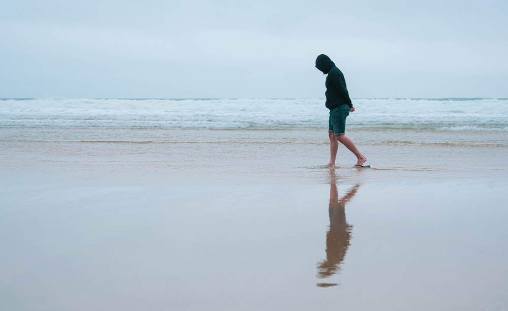 Hombre con chaqueta negra caminando por la playa durante el día