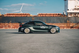 A sleek dark green car being loaded onto a shipping container at a busy port.