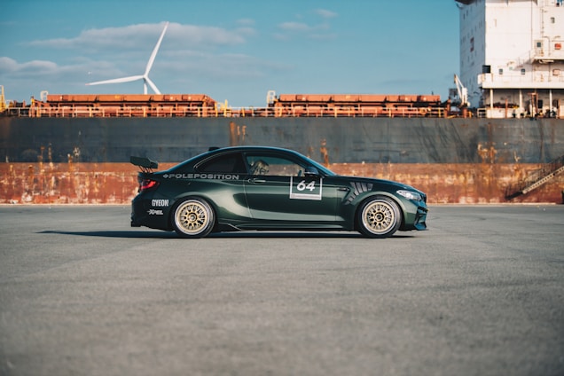 A sleek dark green car being loaded onto a shipping container at a busy port.