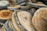 Roughly cut slices of wood with bark edges are stacked atop one another. The surface of each slice exhibits natural wood grain patterns and varying shades of brown.