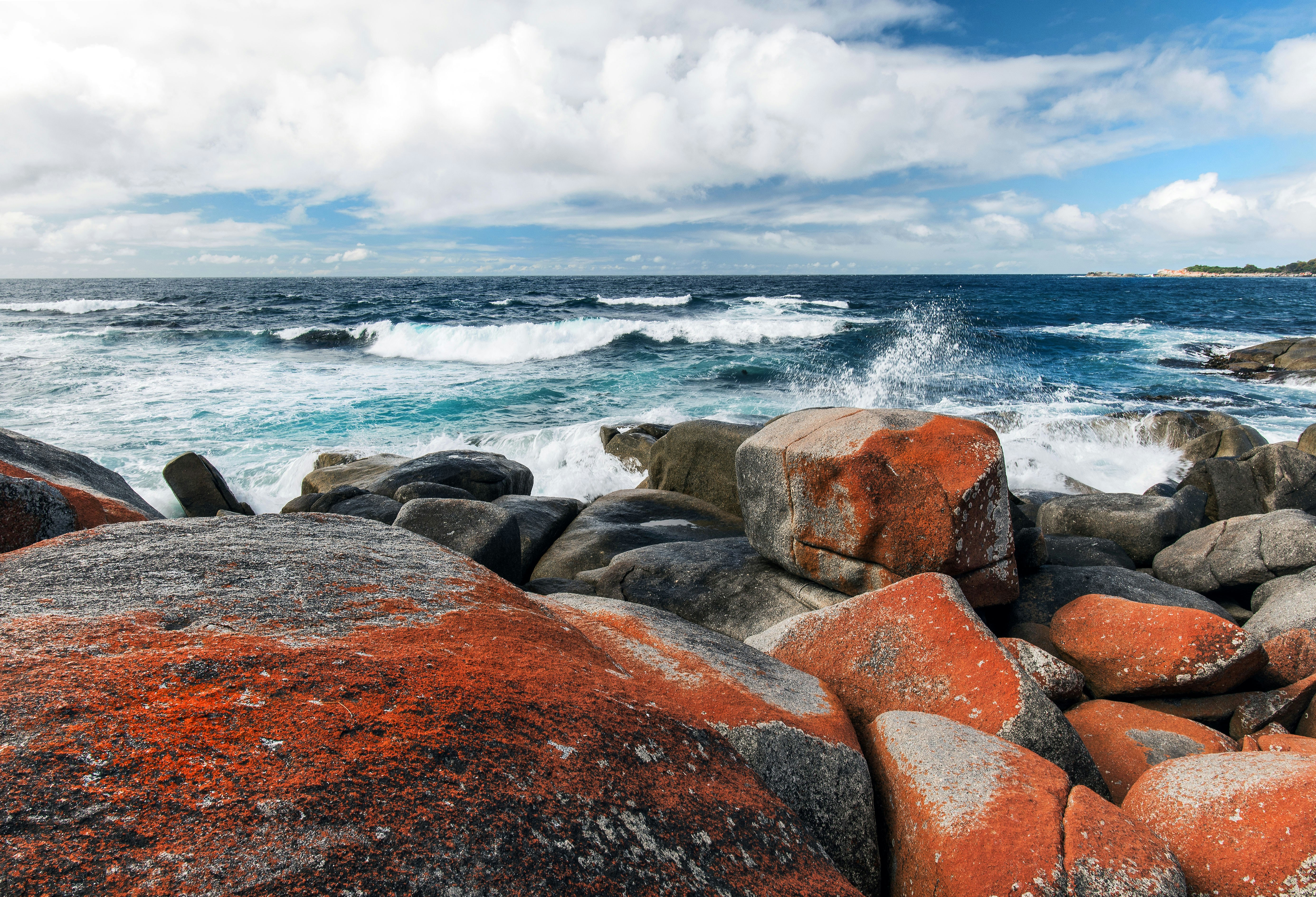 brown and gray rocks near body of water under white clouds during daytime