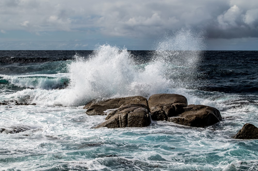 ocean waves crashing on brown rock formation under blue sky during daytime