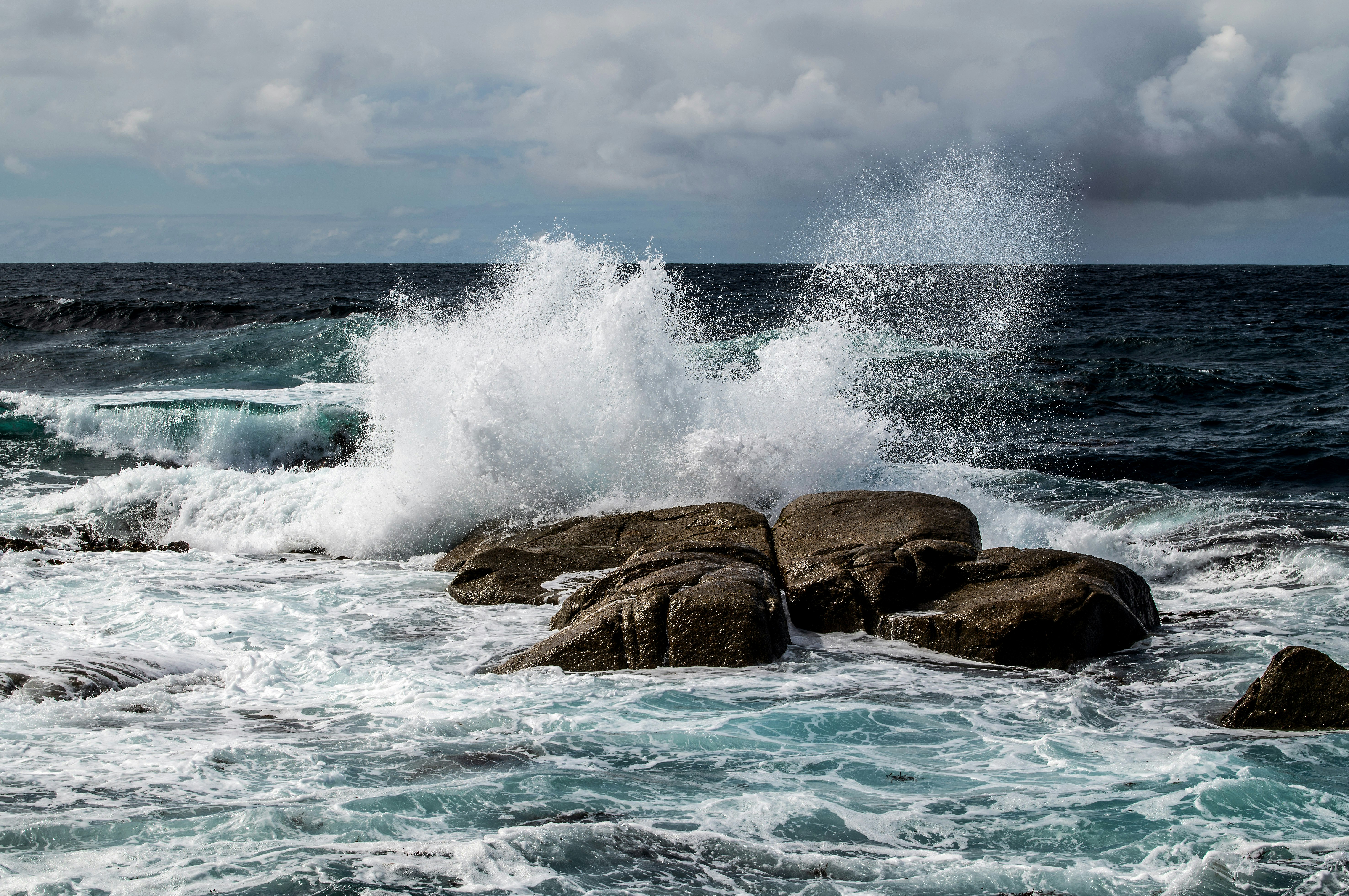 ocean waves crashing on brown rock formation under blue sky during daytime