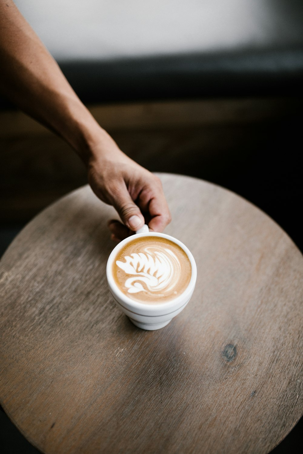 Person hält weiße Keramiktasse mit Cappuccino