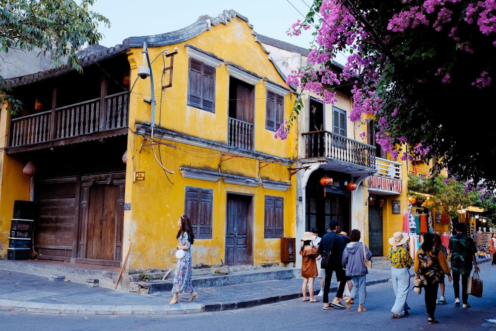 昼間、黄色いコンクリートの建物の近くの歩道を歩く人々