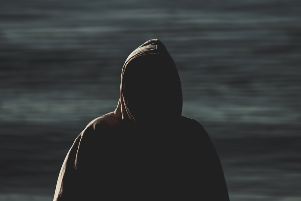 person in black hoodie standing near body of water during daytime