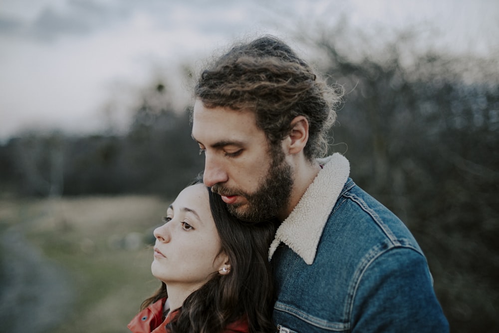 man in blue denim jacket kissing woman in red and black plaid shirt