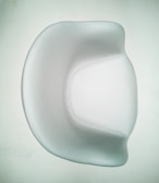 A smooth, modern chair with a minimalist design featuring curved edges and a shiny surface. The chair is predominantly white, set against a pale background, emphasizing its elegant and contemporary style.