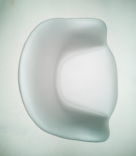 A smooth, modern chair with a minimalist design featuring curved edges and a shiny surface. The chair is predominantly white, set against a pale background, emphasizing its elegant and contemporary style.