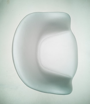 A smooth, modern chair with a minimalist design featuring curved edges and a shiny surface. The chair is predominantly white, set against a pale background, emphasizing its elegant and contemporary style.