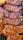 Various cuts of meat are sizzling on a grill, featuring distinct grill marks and a glossy glaze from the sauce. The pieces range in color from deep brown to reddish orange, indicating different levels of cooking and seasoning.