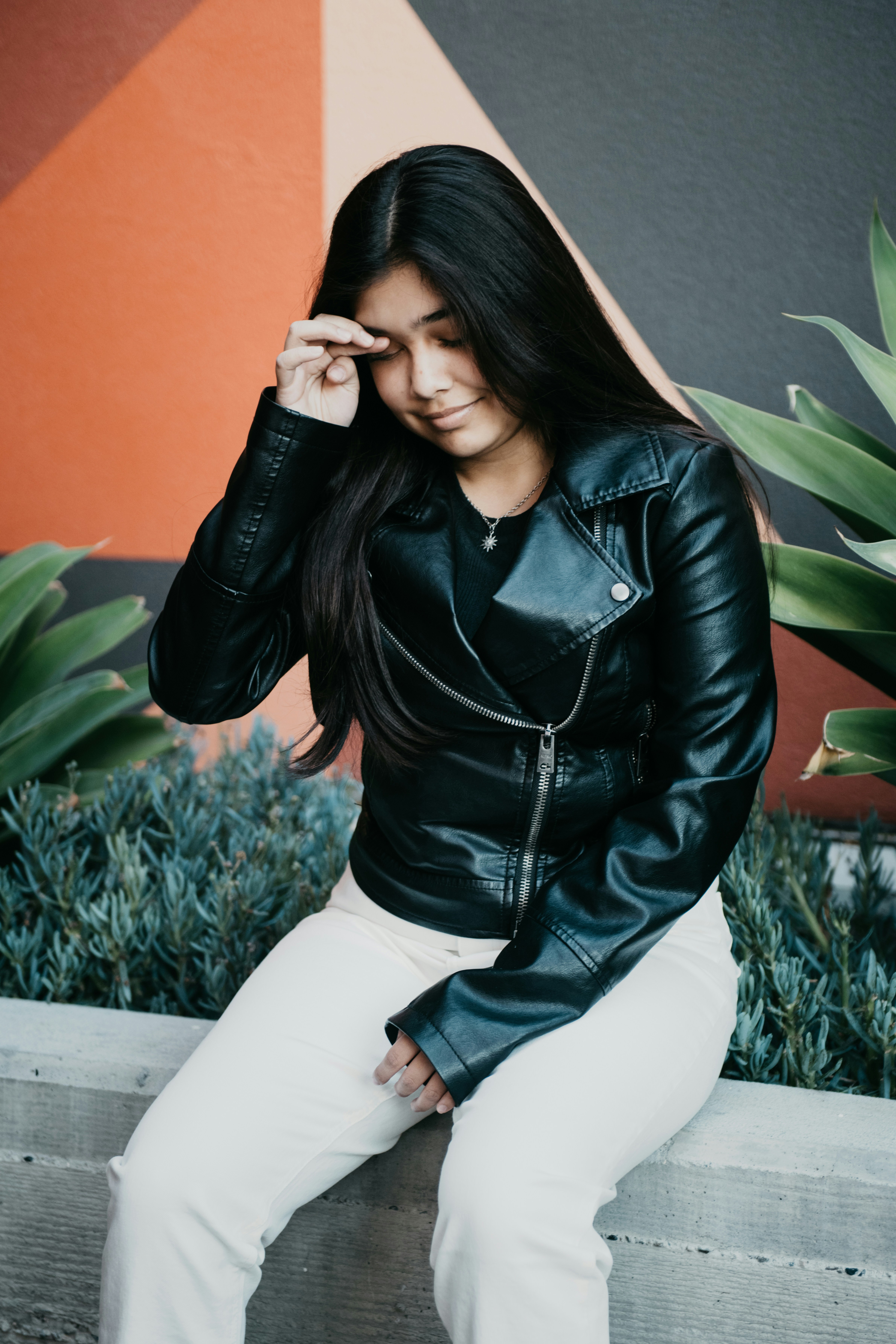 woman in black leather jacket and white pants sitting on white bench