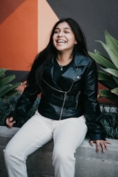 woman in black leather jacket and white pants sitting on green plant