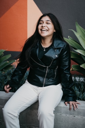 woman in black leather jacket and white pants sitting on green plant