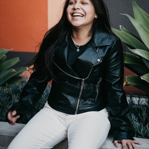 woman in black leather jacket and white pants sitting on green plant