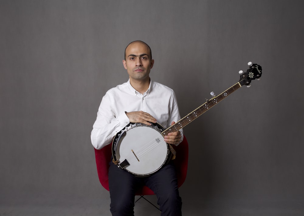 uomo in camicia bianca che suona la chitarra acustica bianca e marrone