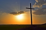 A serene pasture at sunset with a wooden cross standing tall among grazing horses.