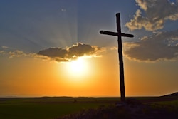 A serene pasture at sunset with a wooden cross standing tall among grazing horses.