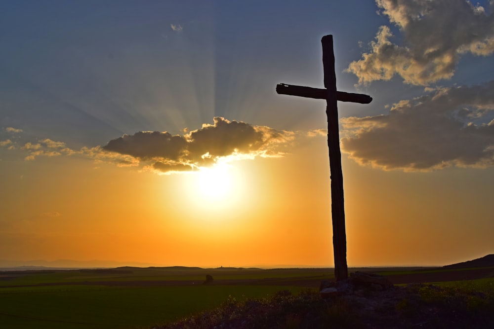 Braunes Holzkreuz auf grünem Grasfeld bei Sonnenuntergang