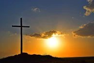 A golden cross standing tall on a hill at sunrise, bathed in divine light.