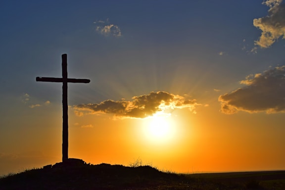 A warm church community gathered around a wooden cross during a sunset.