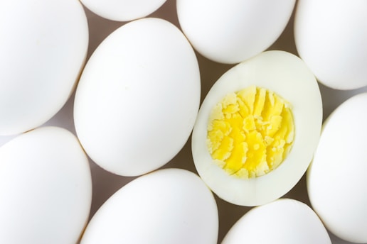 A close-up view of several white eggs with one egg halved to reveal its bright yellow yolk and firm white egg white.
