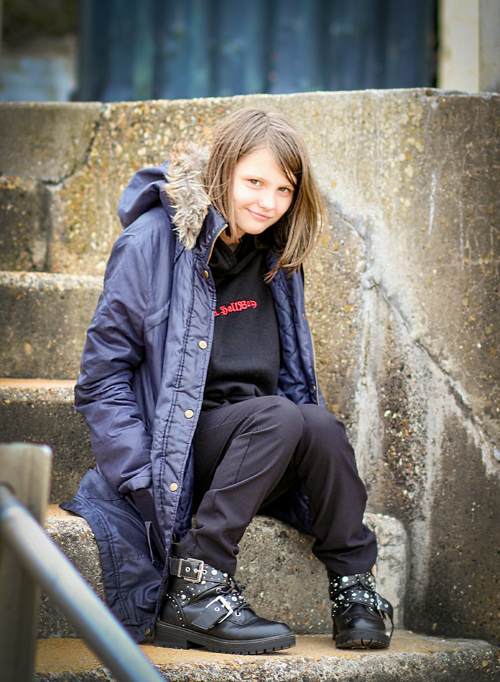 woman in black jacket and black pants sitting on concrete wall