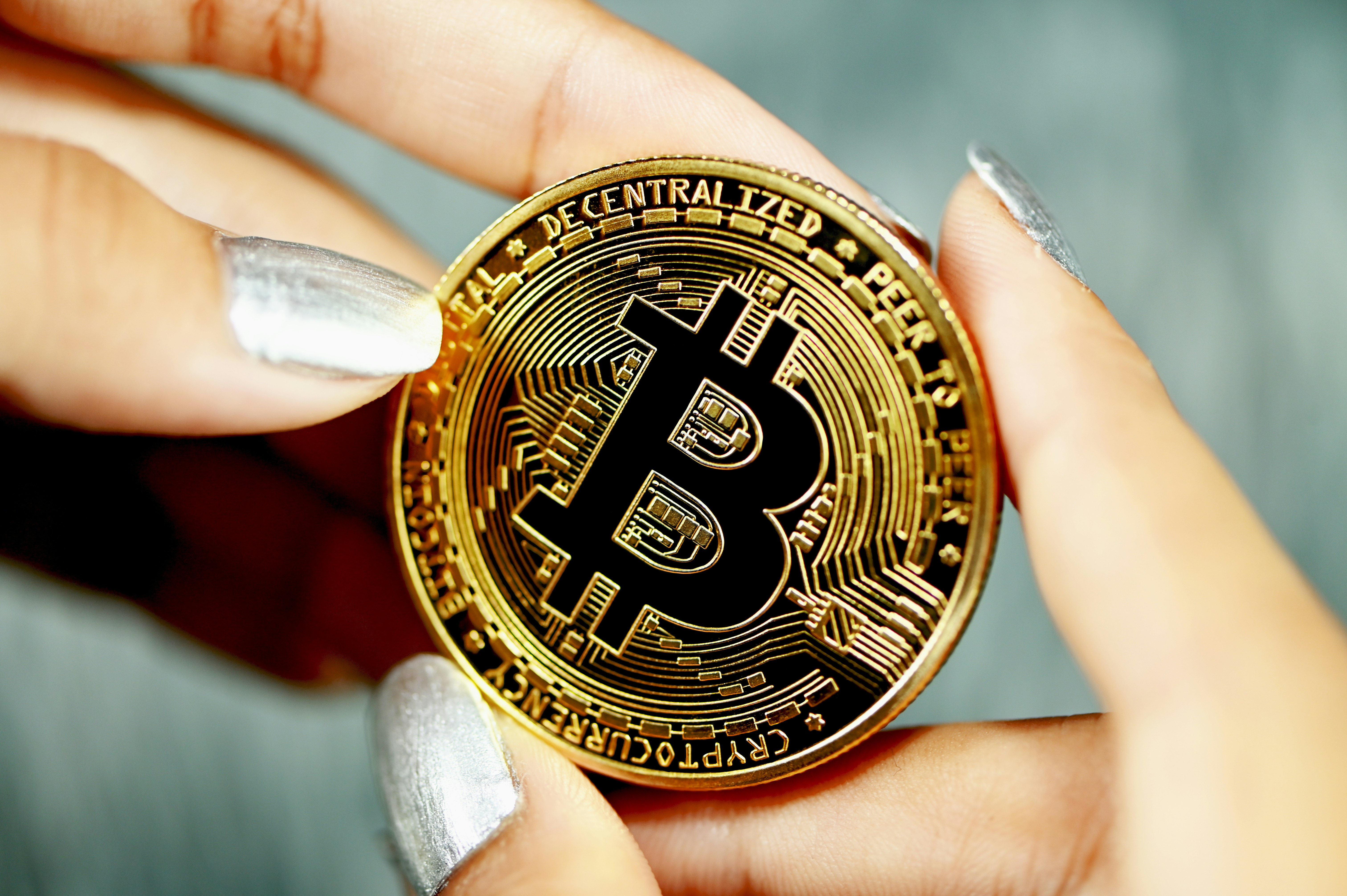 Bitcoin held in both hands with silver-painted nails.
