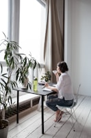 A candid moment of a woman sipping tea by a window, dressed in understated professional attire with a pop of color.