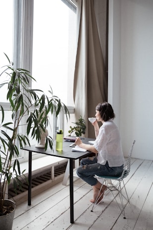 A woman calmly sipping coffee in a minimalist office setting with soft natural light.