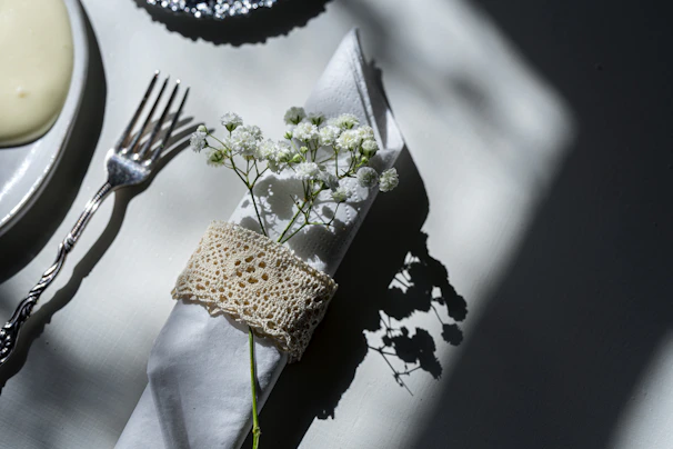 Close-up of a folded napkin with delicate embroidery resting on a smooth ivory tablecloth, evoking refined hospitality.