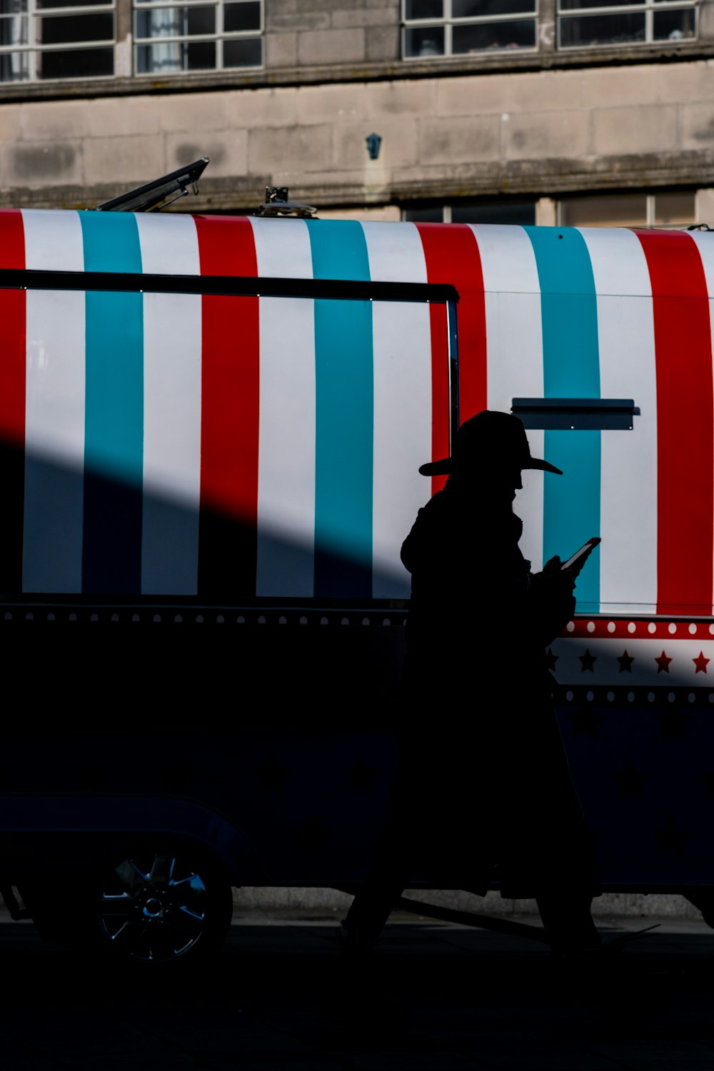 silhouette of man in black jacket standing in front of white red and blue striped wall