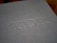 A close-up of a gray textured surface with embossed uppercase letters TDR. The surface has a fabric-like appearance, suggesting it might be the cover of a book or an album.