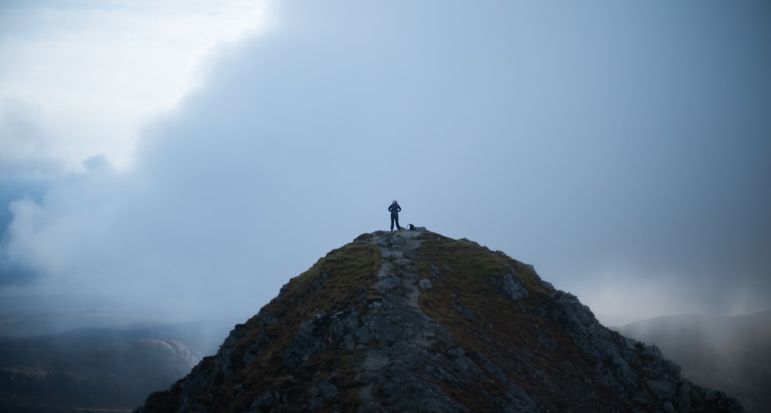 person standing on rock formation under white clouds during daytime