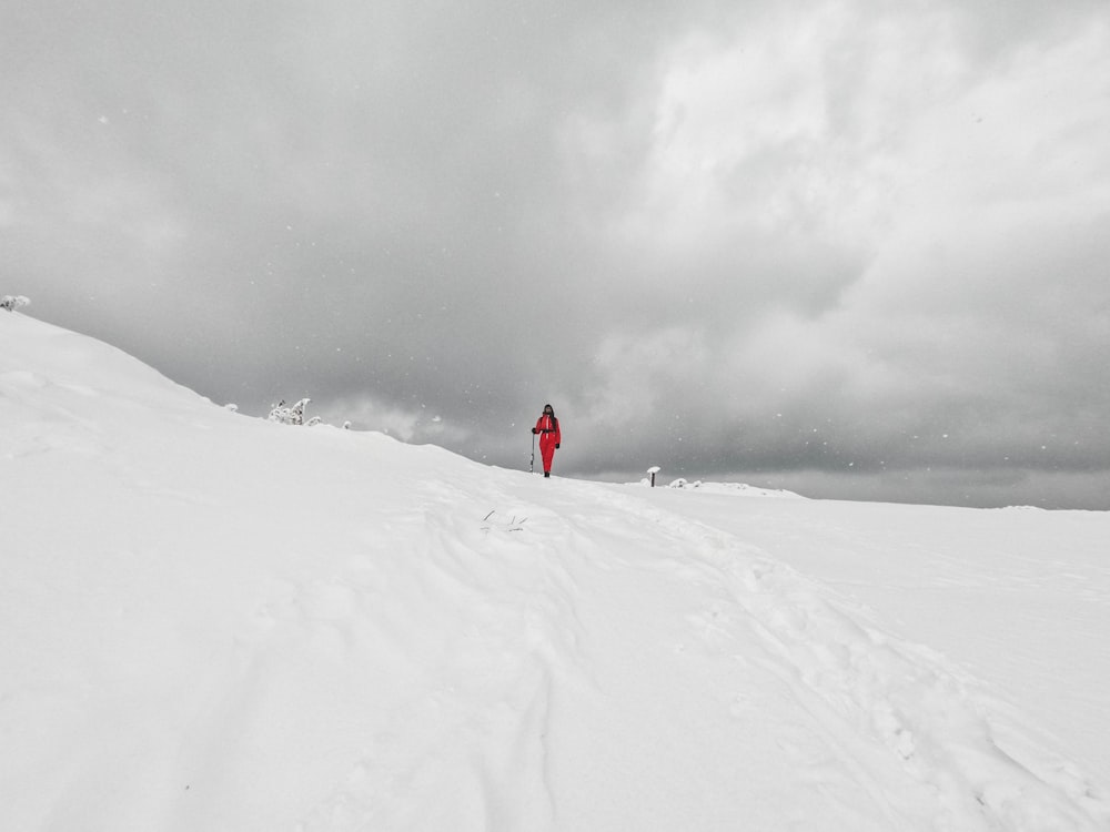 person in red jacket and black pants walking on snow covered ground during daytime