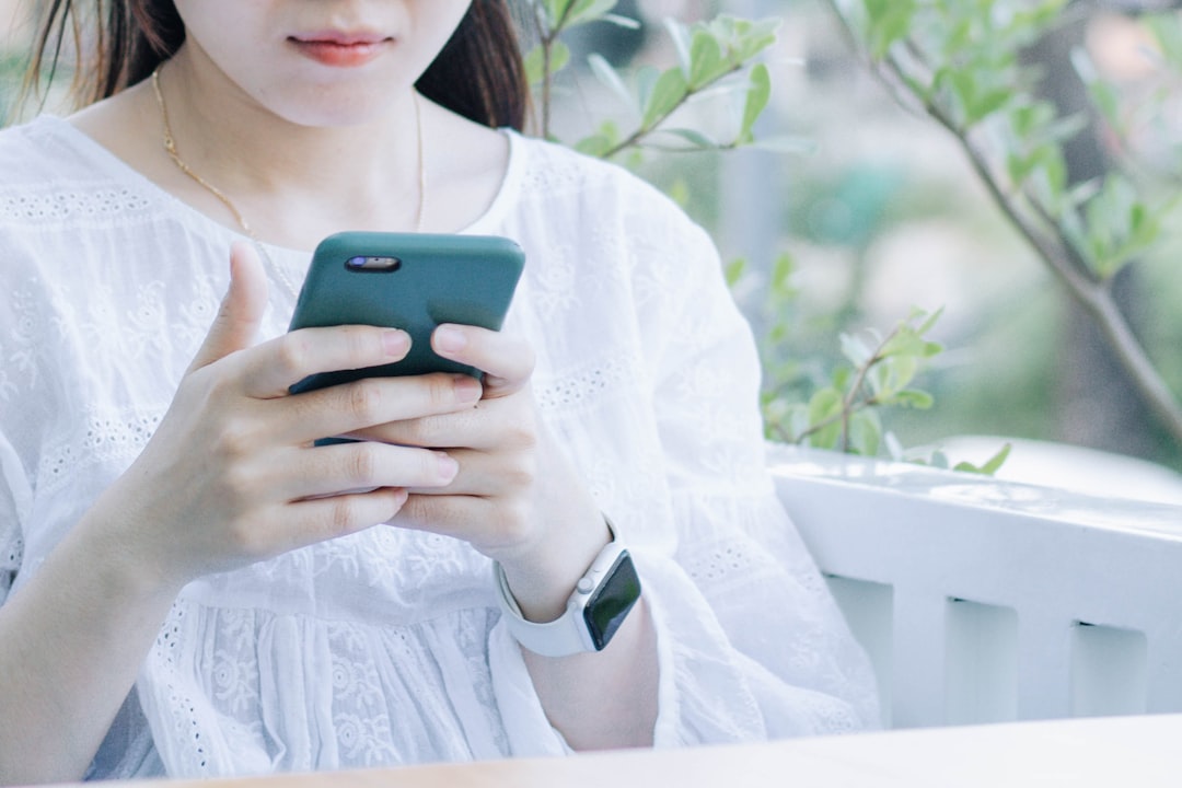 woman in white and blue floral dress holding green smartphone